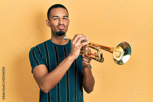 Sticker Young african american man playing trumpet looking at the camera blowing a kiss being lovely and sexy
