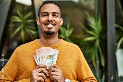 Young african american man smiling happy holding new zealand dollars at the city. photo