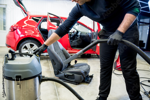 Car service worker cleaning car seat with vacuum cleaner.