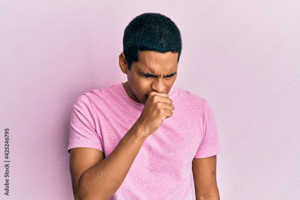 Young handsome hispanic man wearing casual pink t shirt feeling unwell and coughing as symptom for cold or bronchitis. health care concept. Young handsome hispanic man wearing casual pink t shirt feeling unwell and coughing as symptom for cold or bronchitis. health care concept.