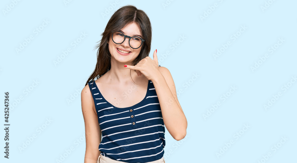 Young beautiful caucasian girl wearing casual clothes and glasses smiling doing phone gesture with hand and fingers like talking on the telephone. communicating concepts.