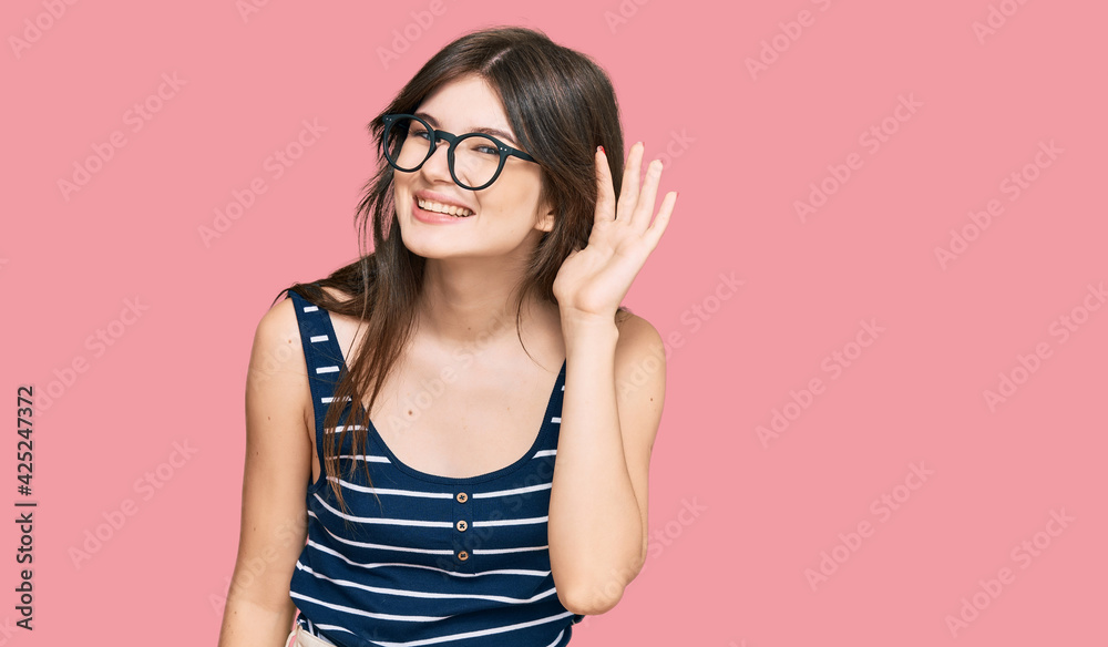 Young beautiful caucasian girl wearing casual clothes and glasses smiling with hand over ear listening an hearing to rumor or gossip. deafness concept. Young beautiful caucasian girl wearing casual clothes and glasses smiling with hand over ear listening an hearing to rumor or gossip. deafness concept.