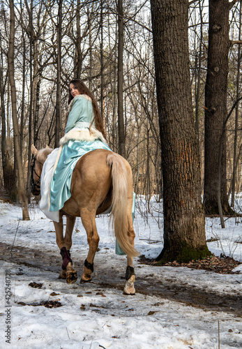 beautiful girl in a blue outfit and a light brown horse in a spring forest