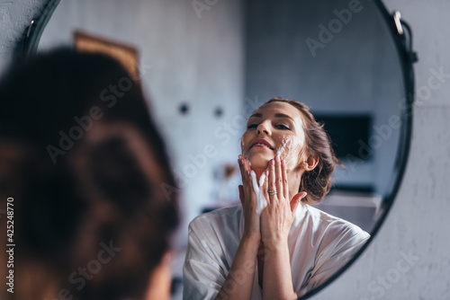 Woman in the bathroom washing her face with foam photo