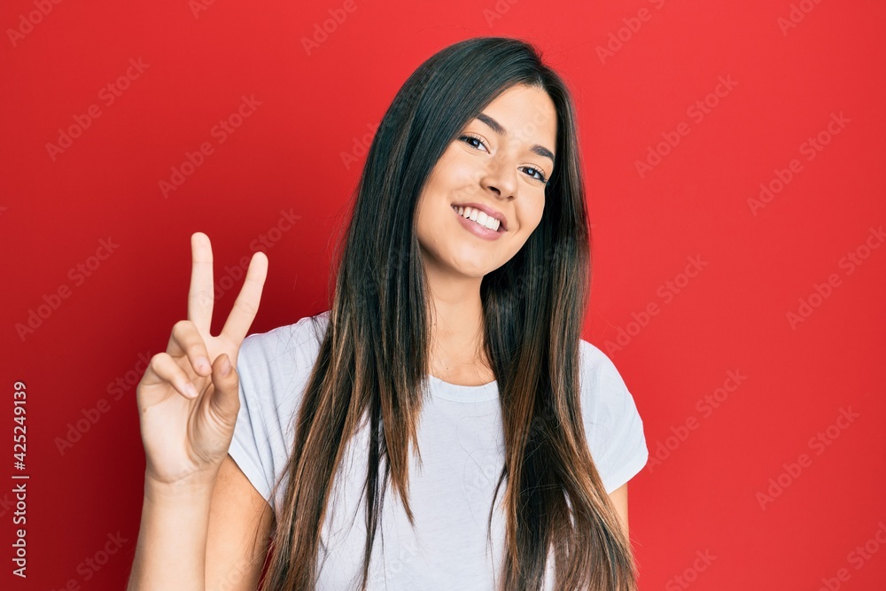 Young brunette woman wearing casual white tshirt over red background showing and pointing up with fingers number two while smiling confident and happy. Young brunette woman wearing casual white tshirt over red background showing and pointing up with fingers number two while smiling confident and happy.