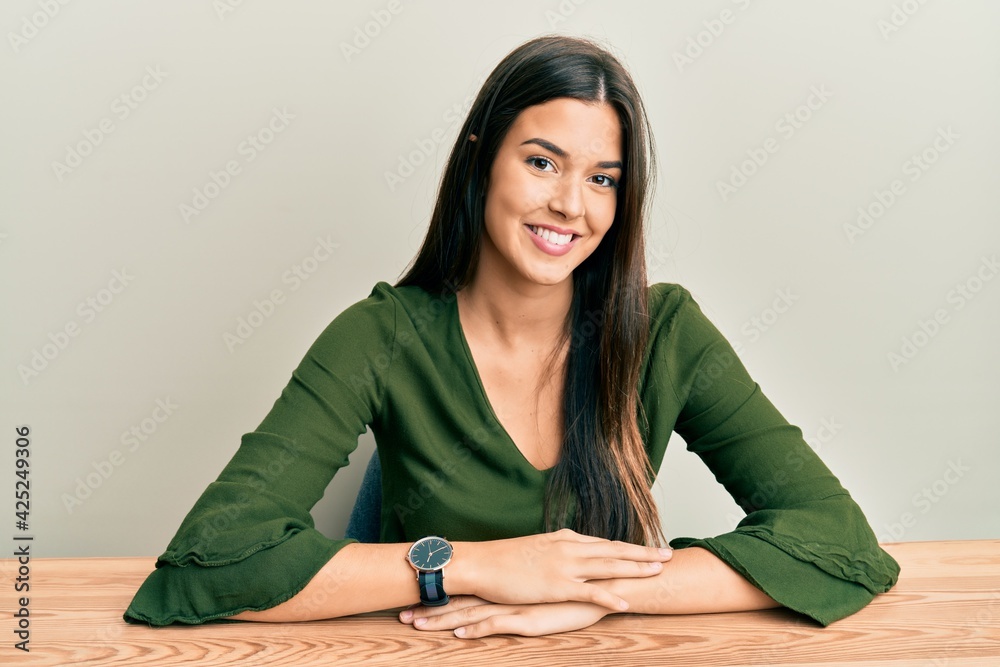 Young brunette woman wearing casual clothes sitting on the table with a happy and cool smile on face. lucky person. Young brunette woman wearing casual clothes sitting on the table with a happy and cool smile on face. lucky person.