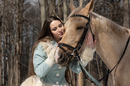 beautiful girl in a blue outfit and a light brown horse in a spring forest