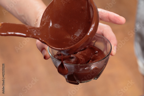 Pouring dark melted chocolate in a glass bowl.
