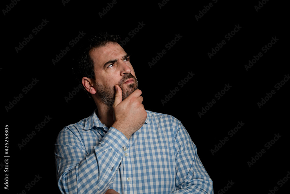 Portrait of handsome bearded man in a blue and white plaid shirt with his hand on his chin with thoughtful gesture on black studio background Portrait of handsome bearded man in a blue and white plaid shirt with his hand on his chin with thoughtful gesture on black studio background
