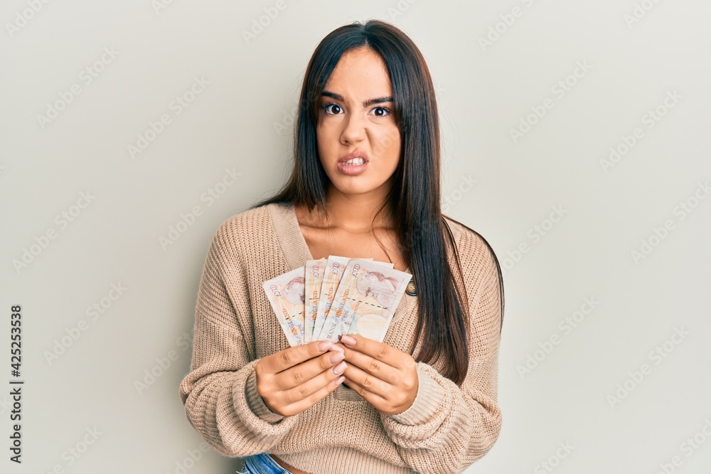 Young beautiful hispanic girl holding 10 united kingdom pounds banknotes clueless and confused expression. doubt concept. Young beautiful hispanic girl holding 10 united kingdom pounds banknotes clueless and confused expression. doubt concept.