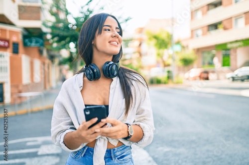 Young hispanic girl smiling happy using smartphone and headphones at the city. © Krakenimages.com