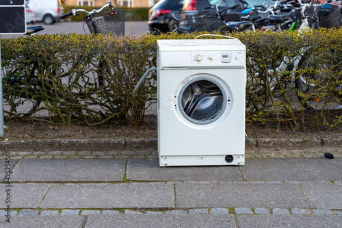 Washing machine standing outside near a hedge on a spring day