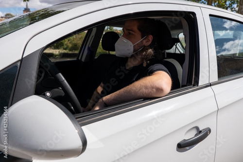 Young guy with long hair wearing a face mask by COVID-19 driving © Jennifer