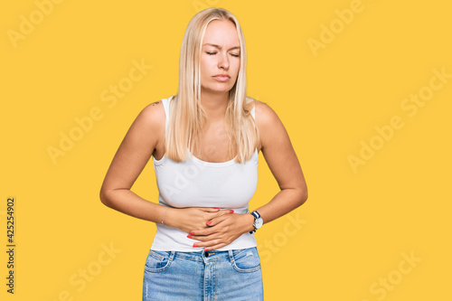 Young blonde girl wearing casual style with sleeveless shirt with hand on stomach because indigestion, painful illness feeling unwell. ache concept.