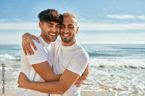 Young gay couple smiling happy hugging at the beach.