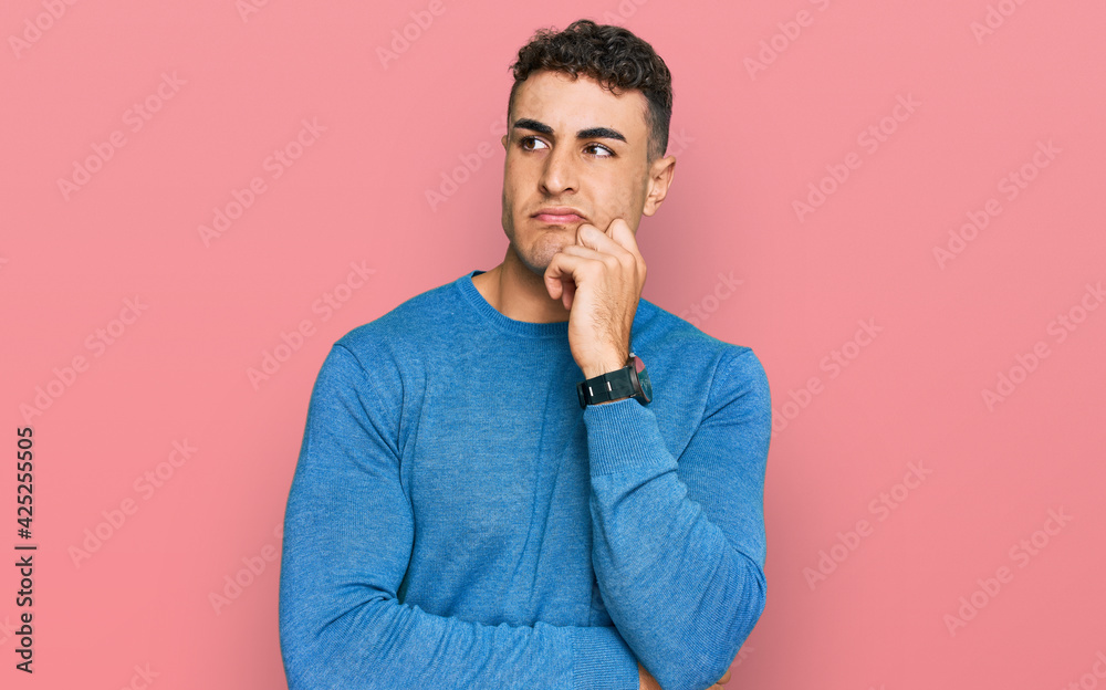 Hispanic young man wearing casual clothes serious face thinking about question with hand on chin, thoughtful about confusing idea Hispanic young man wearing casual clothes serious face thinking about question with hand on chin, thoughtful about confusing idea