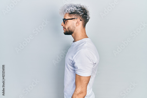 Young hispanic man with modern dyed hair wearing white t shirt and glasses looking to side, relax profile pose with natural face and confident smile. photo