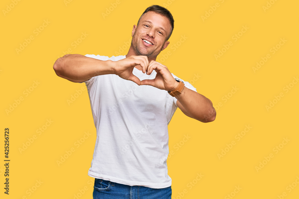 Handsome muscle man wearing casual white tshirt smiling in love doing heart symbol shape with hands. romantic concept. Handsome muscle man wearing casual white tshirt smiling in love doing heart symbol shape with hands. romantic concept.