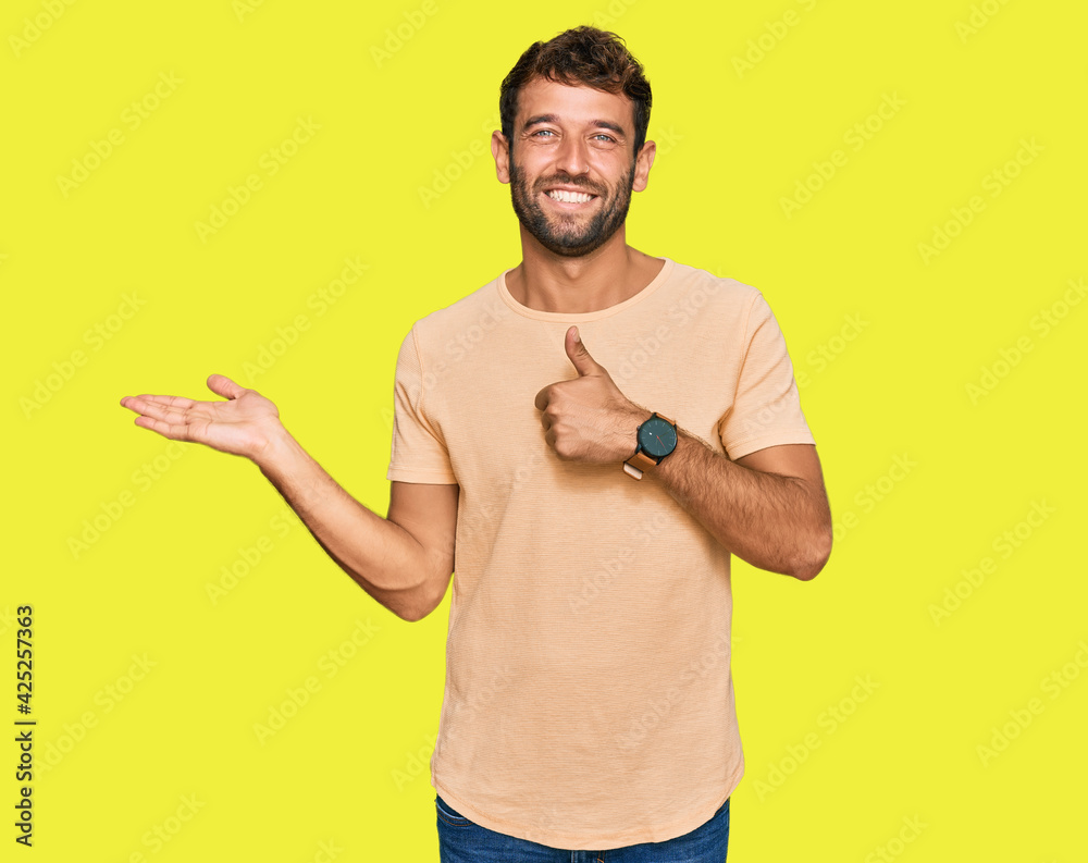 Handsome young man with beard wearing casual tshirt showing palm hand and doing ok gesture with thumbs up, smiling happy and cheerful Handsome young man with beard wearing casual tshirt showing palm hand and doing ok gesture with thumbs up, smiling happy and cheerful