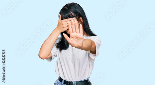 Young hispanic girl wearing casual clothes covering eyes with hands and doing stop gesture with sad and fear expression. embarrassed and negative concept.