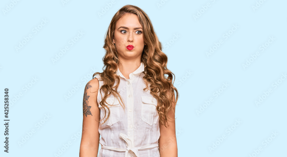 Young blonde girl wearing casual clothes puffing cheeks with funny face. mouth inflated with air, crazy expression.