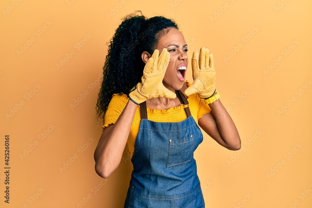 Middle age african american woman wearing professional apron shouting angry out loud with hands over mouth Middle age african american woman wearing professional apron shouting angry out loud with hands over mouth