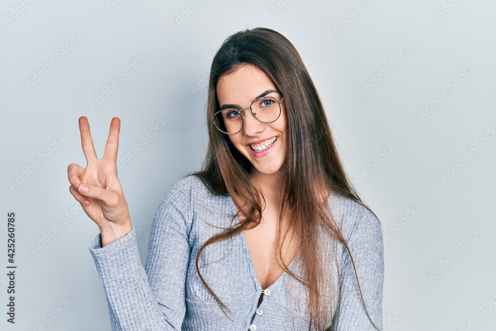 Young brunette teenager wearing casual sweater and glasses smiling with happy face winking at the camera doing victory sign. number two. Young brunette teenager wearing casual sweater and glasses smiling with happy face winking at the camera doing victory sign. number two.