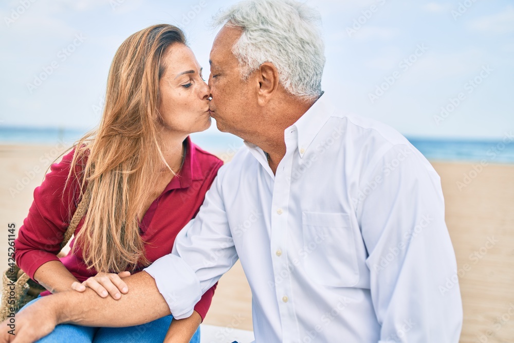 Obraz premium Middle age hispanic couple smiling happy sitting on bench at the beach.