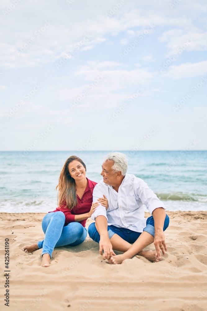 Middle age hispanic couple smiling happy and hugging sitting at the beach Middle age hispanic couple smiling happy and hugging sitting at the beach