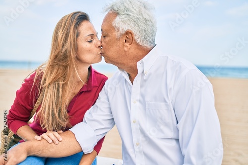 Middle age hispanic couple smiling happy sitting on bench at the beach.