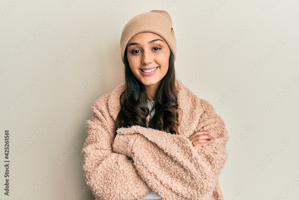Young hispanic woman wearing wool sweater and winter hat happy face smiling with crossed arms looking at the camera. positive person.