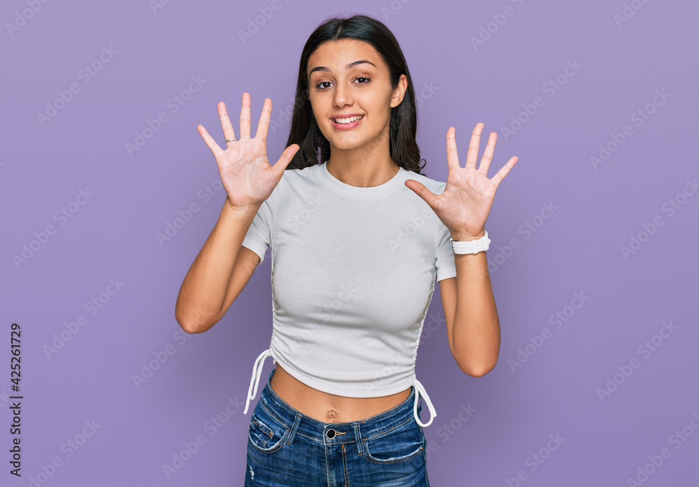 Young hispanic girl wearing casual white t shirt showing and pointing up with fingers number ten while smiling confident and happy.