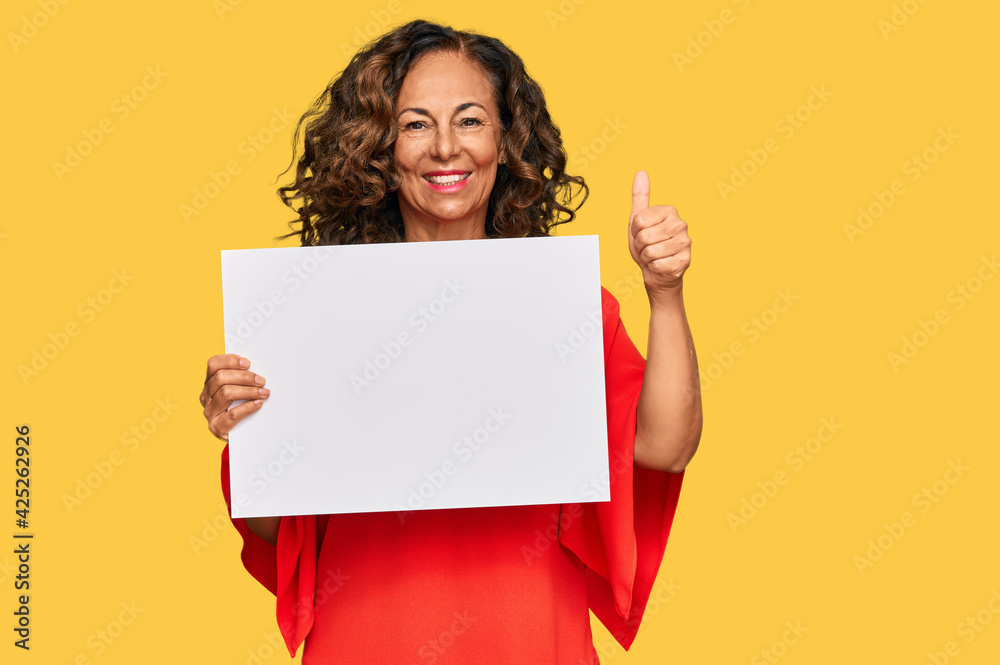 Middle age hispanic woman holding blank empty banner smiling happy and positive, thumb up doing excellent and approval sign Middle age hispanic woman holding blank empty banner smiling happy and positive, thumb up doing excellent and approval sign