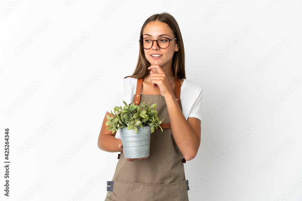 Gardener girl holding a plant over isolated white background looking to the side and smiling Gardener girl holding a plant over isolated white background looking to the side and smiling