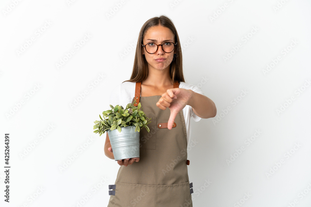 Gardener girl holding a plant over isolated white background showing thumb down with negative expression Gardener girl holding a plant over isolated white background showing thumb down with negative expression