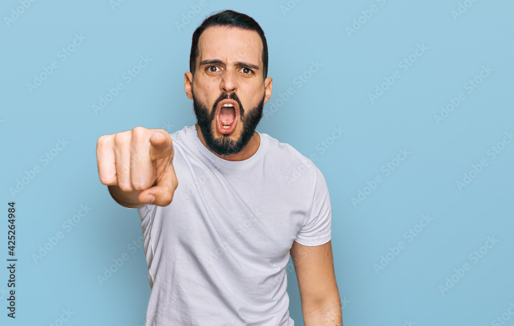 Young man with beard wearing casual white t shirt pointing displeased and frustrated to the camera, angry and furious with you Young man with beard wearing casual white t shirt pointing displeased and frustrated to the camera, angry and furious with you