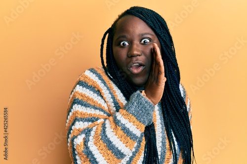 Young black woman with braids wearing casual winter sweater hand on mouth telling secret rumor, whispering malicious talk conversation © Krakenimages.com