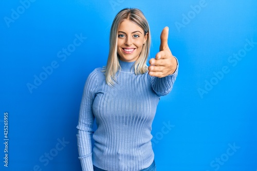 Beautiful blonde woman wearing casual clothes smiling friendly offering handshake as greeting and welcoming. successful business.