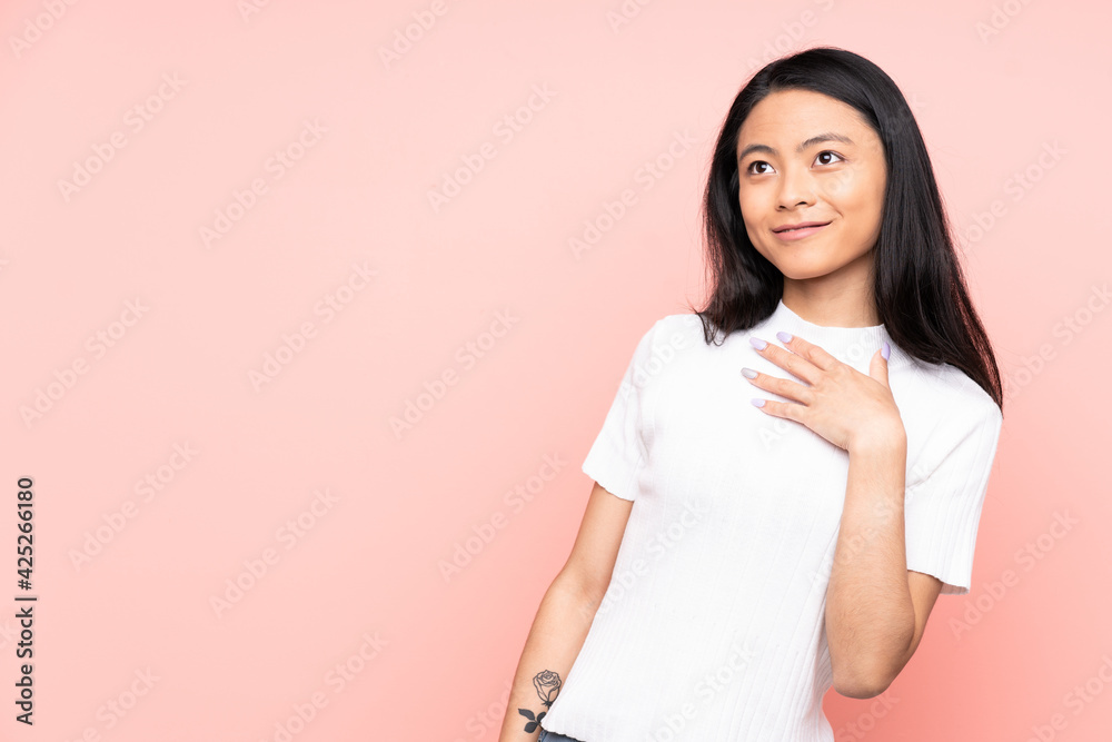 Teenager Chinese woman isolated on pink background looking up while smiling