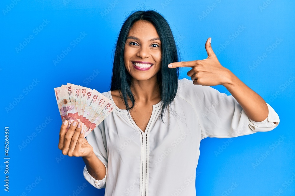 Young african american woman holding 10 colombian pesos banknotes smiling cheerful showing and pointing with fingers teeth and mouth. dental health concept. Young african american woman holding 10 colombian pesos banknotes smiling cheerful showing and pointing with fingers teeth and mouth. dental health concept.