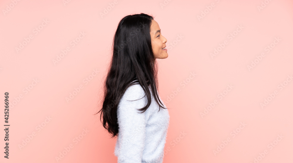 Teenager Chinese woman isolated on pink background laughing in lateral position