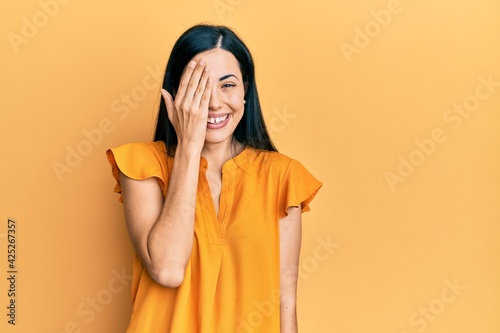 Beautiful young woman wearing casual clothes covering one eye with hand, confident smile on face and surprise emotion. © Krakenimages.com