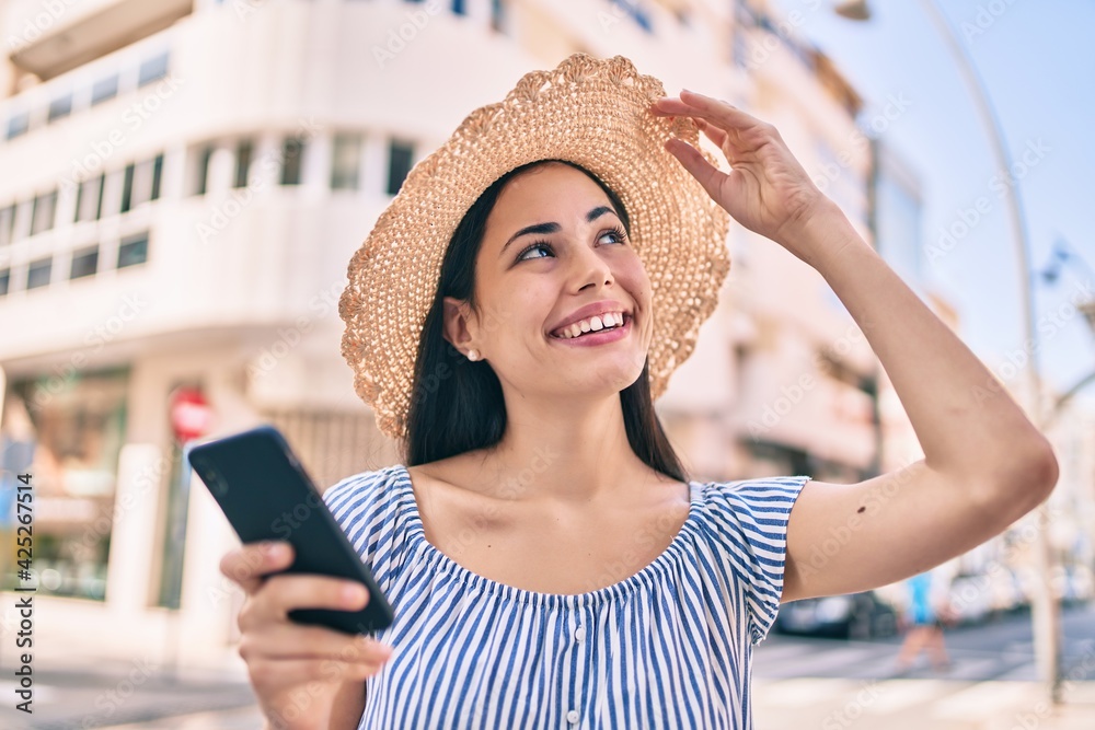 Young latin tourist girl on vacation smiling happy  using smartphone at the city.