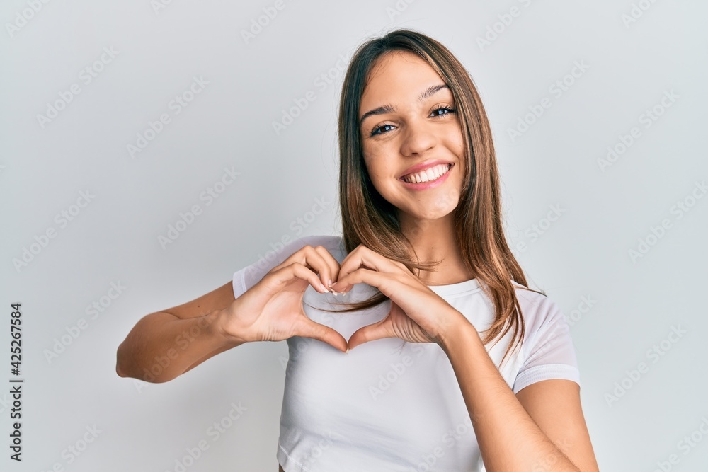 Young brunette woman wearing casual white t shirt smiling in love doing heart symbol shape with hands. romantic concept. Young brunette woman wearing casual white t shirt smiling in love doing heart symbol shape with hands. romantic concept.