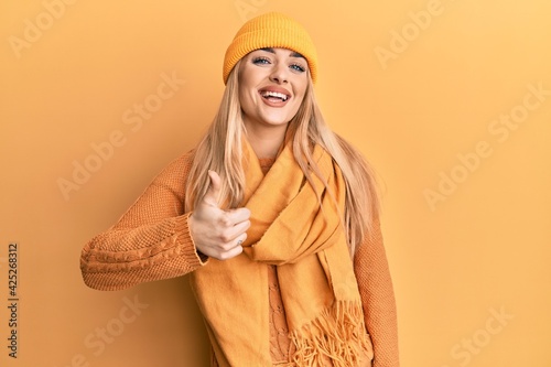 Young caucasian woman wearing wool winter sweater and cap doing happy thumbs up gesture with hand. approving expression looking at the camera showing success. © Krakenimages.com