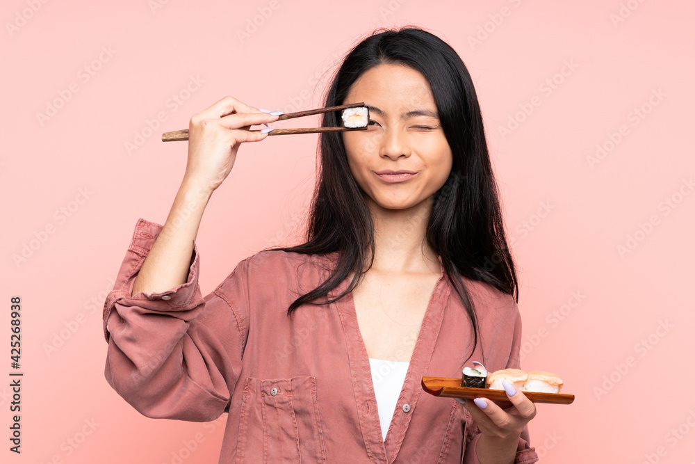 Teenager Asian girl eating sushi isolated on pink background Teenager Asian girl eating sushi isolated on pink background