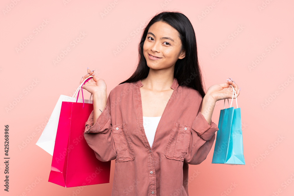 Teenager Chinese girl isolated on pink background holding shopping bags and smiling