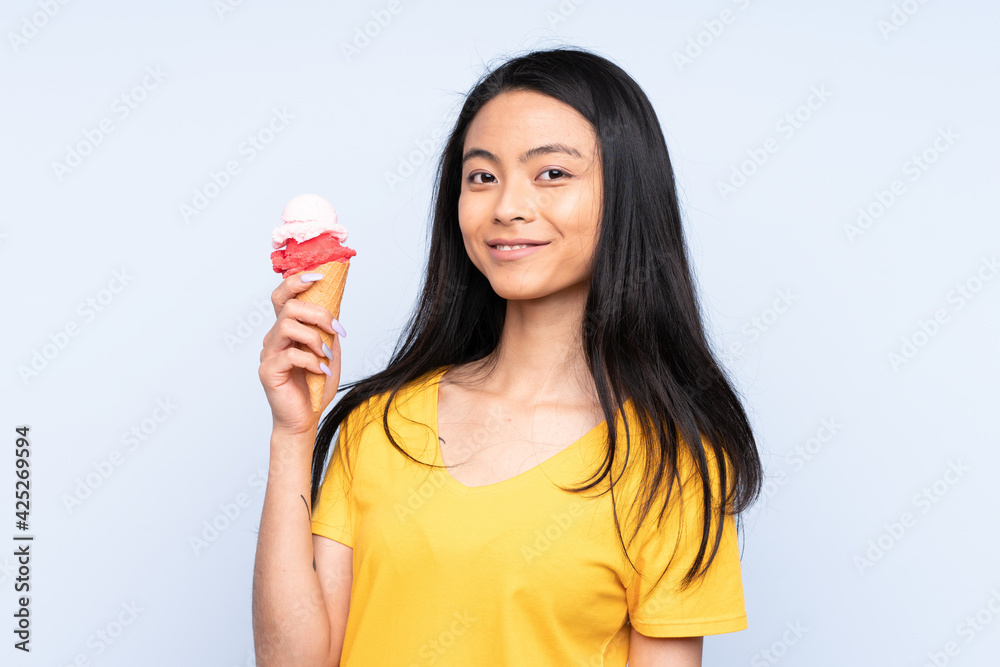 Teenager Asian girl with a cornet ice cream isolated on blue background Teenager Asian girl with a cornet ice cream isolated on blue background