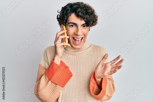Hispanic young man having conversation talking on the smartphone celebrating victory with happy smile and winner expression with raised hands