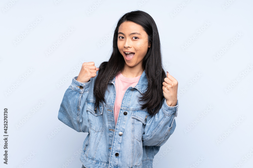 Teenager Chinese woman isolated on blue background celebrating a victory in winner position Teenager Chinese woman isolated on blue background celebrating a victory in winner position